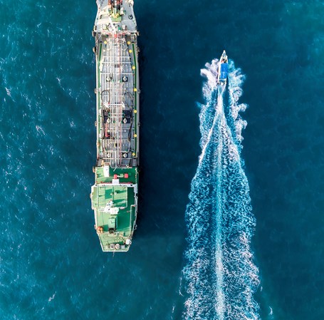 Containerskib og speedbåd sejler langs hinanden på havet.